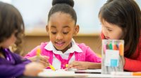 A small group of elementary students writing together on the same piece of paper