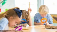 A photo of elementary students examining natural materials with magnifying glasses