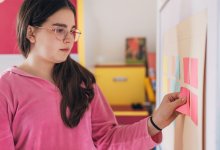 A middle school student attaching a sticky note to a classroom's whiteboard