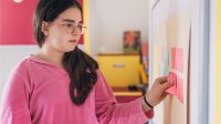 A middle school student attaching a sticky note to a classroom's whiteboard